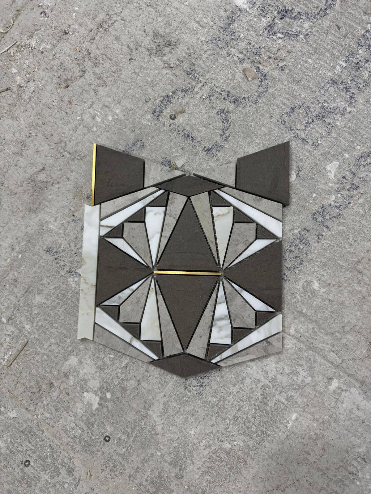 A gray and white geometric tile sample is held over a rough floor.