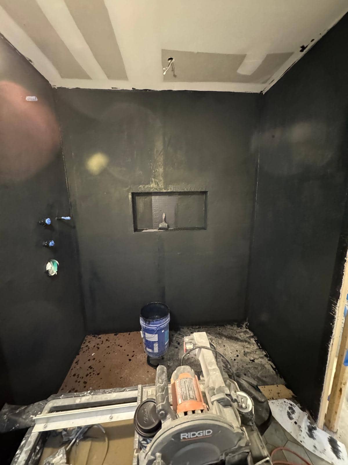 The dark coating on these shower walls is part of construction preparation, not a decorative paint finish.