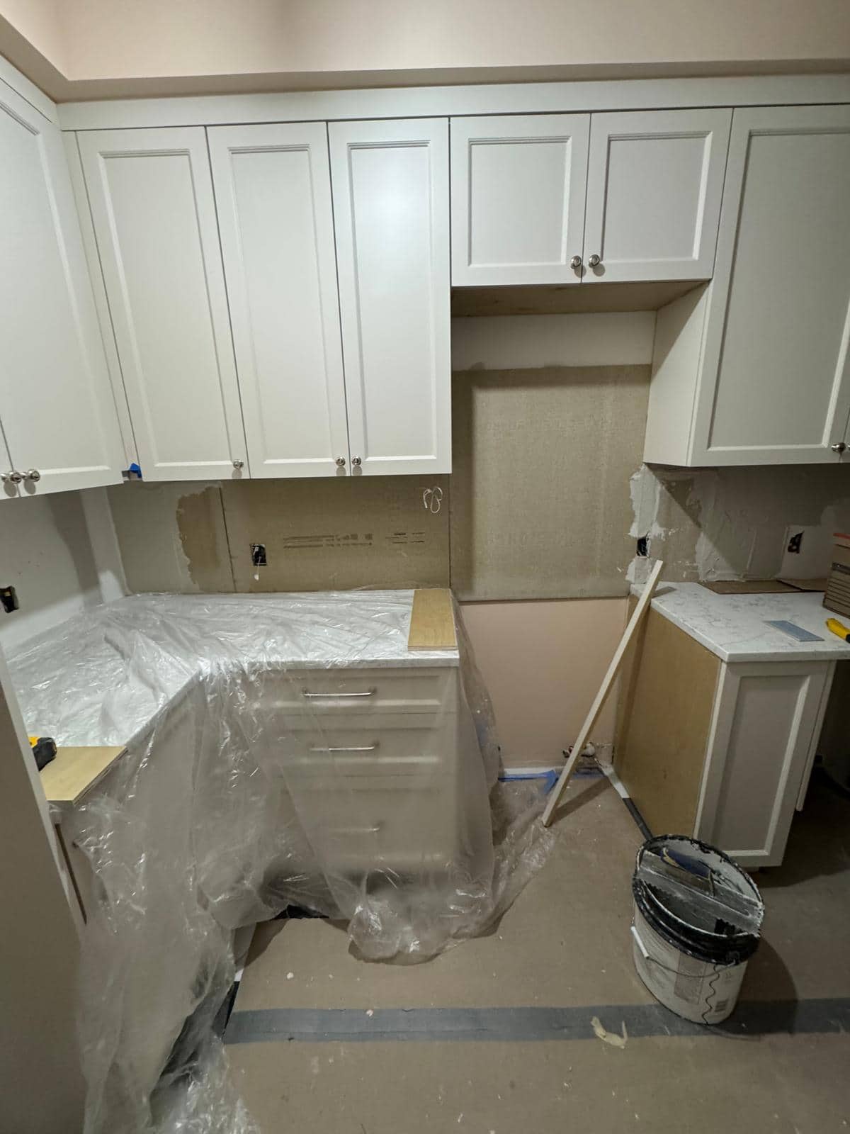 Protective covering remains near cream kitchen cabinetry in this photo.