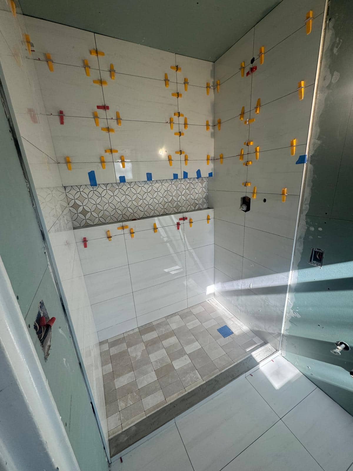 Large-format bathroom wall tile with decorative shower niche band.