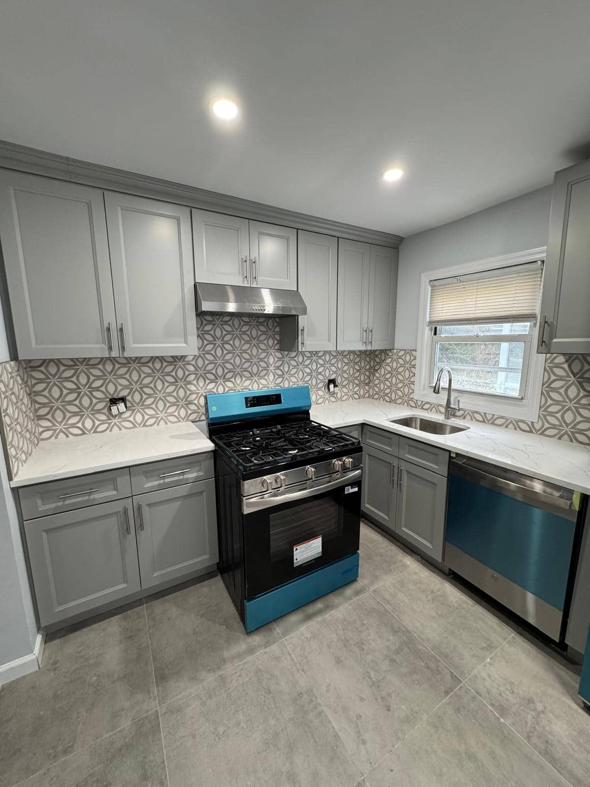 Gray kitchen cabinets with patterned backsplash and new flooring.