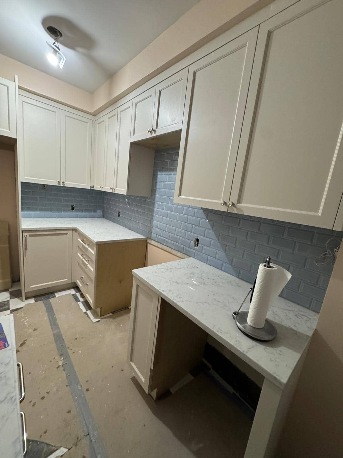 This angle shows cream cabinet fronts, a blue backsplash, and protection still covering the floor.